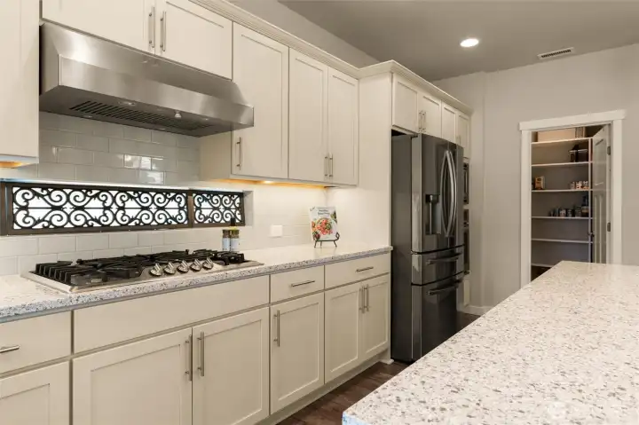 A gourmet centerpiece featuring a five-burner gas cooktop and high-powered exhaust fan, conveniently located near the refrigerator, built-in oven, and microwave