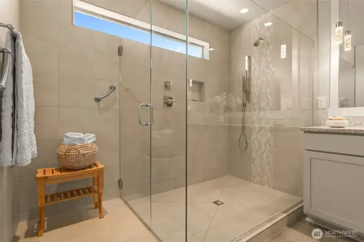 This primary bath features a walk-in tiled shower with two shower heads and an area to undress, all illuminated by natural light