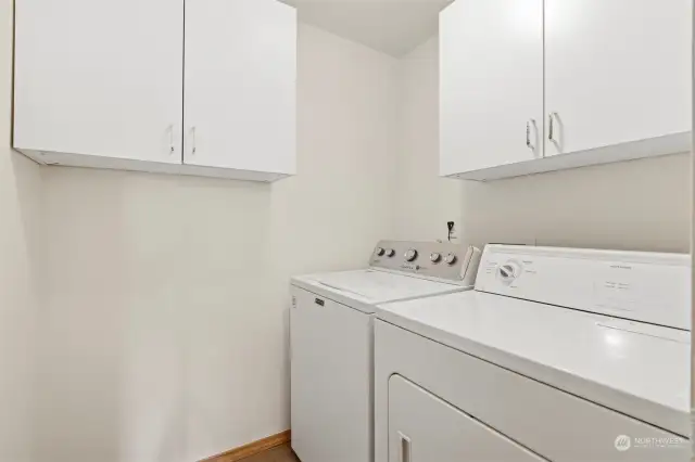 The laundry room has a washer and dryer as well as some cabinet storage.