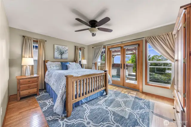 The primary bedroom offers a serene escape with warm wood tones, a ceiling fan, and French doors leading directly to the deck and hot tub. Wake up to filtered sunlight and the tranquility of a coastal breeze.