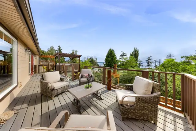 Step out onto the elevated composite deck, surrounded by evergreens and overlooking glimpses of Birch Bay. The outdoor lounge area with wicker-style seating offers a peaceful haven for morning coffee or sunset chats.