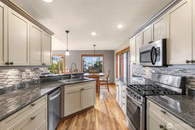 The kitchen dazzles with granite countertops, stainless steel appliances, gas range, and a mosaic tile backsplash. An open bar area makes entertaining effortless while soaking in views toward the deck and dining area.