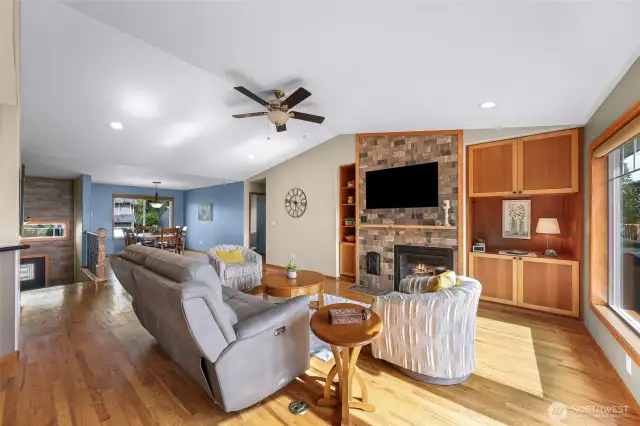 A second angle of the living room highlights the integration of comfort and craftsmanship, featuring built-in shelving, a stone hearth, and plush seating—perfect for evenings by the fire. The layout blends naturally into the dining space beyond.