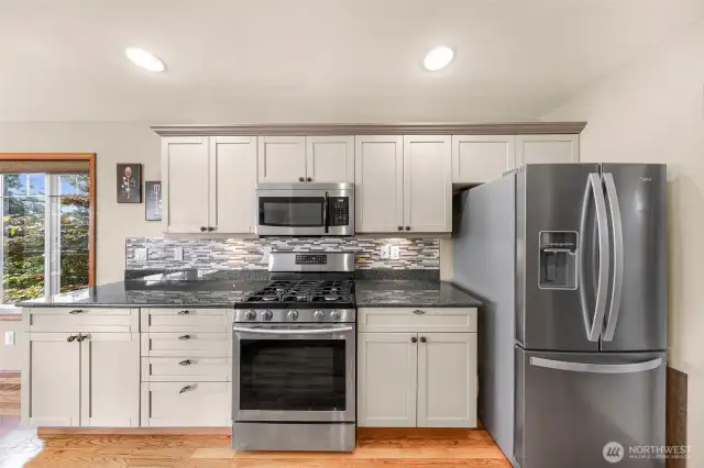 This straight-on view showcases the stainless steel appliance suite—including a gas range and microwave—accented by soft-close cabinetry and sleek mosaic tile for a contemporary, polished look.