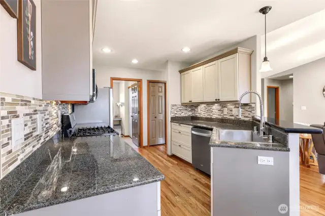 A spacious galley layout and warm hardwood floors create ease of movement in this updated kitchen, featuring ample prep space, stylish backsplash, and open sightlines to the dining and living areas.