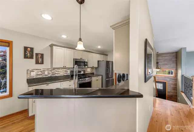 This angled view of the kitchen reveals a beautiful contrast between the dark granite countertops and creamy cabinetry. The raised breakfast bar and pendant lighting create a functional space ideal for entertaining.