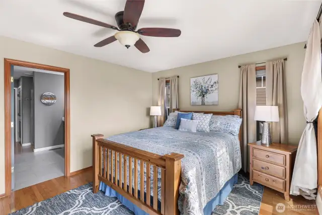 The primary bedroom is generously sized with ample wall space, hardwood floors, and ceiling fan comfort—anchoring the home with quiet sophistication and a connection to the backyard.