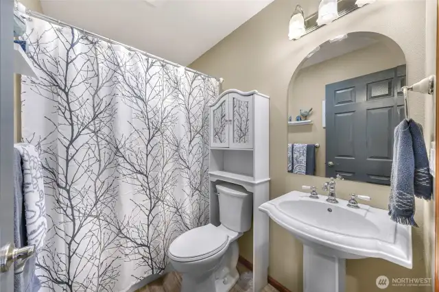 A calming full bathroom with soft neutral tones, pedestal sink, and charming tree-branch shower curtain brings both function and visual interest to this updated space.