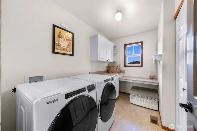 The bright laundry room includes front-loading Whirlpool washer/dryer, extra counter space, a window for light, and built-in seating—designed for comfort and efficiency.
