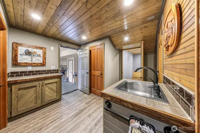 This lower-level bonus area offers flexible utility with wood detailing, wet bar, and direct access to the garage—perfect as a creative studio, kitchenette, or guest prep space.
