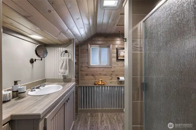 A cozy and rustic full bath with wood paneling, corrugated metal trim, and a walk-in shower brings cabin-like warmth and utility to the lower level.