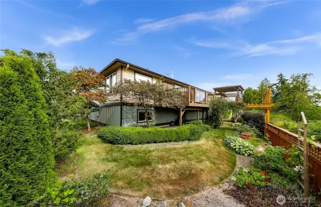 The backyard is a lush, terraced oasis with manicured landscaping, mature trees, and flowering shrubs—creating a private escape in the heart of the gated Sealinks community.
