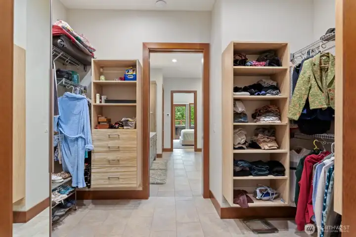 Walk in in primary closet with custom shelving and drawers open to laundry room and back hall for easy living.