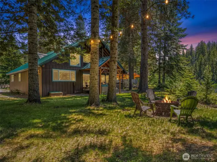 As evening settles in, this riverfront retreat transforms into a warm and inviting mountain escape. String lights drape through the towering evergreens, while the fire pit gathering area creates the perfect setting for sharing stories beneath the stars As evening settles in, this riverfront retreat transforms into a warm and inviting mountain escape. String lights drape through the towering evergreens, while the fire pit gathering area creates the perfect setting for sharing stories beneath the stars