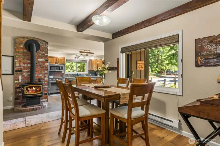 Cozy dining area with exposed beams, wood stove on a brick hearth, warm wood flooring, and large windows overlooking the surrounding trees. Open to the kitchen for easy entertaining and everyday living. Cozy dining area with exposed beams, wood stove on a brick hearth, warm wood flooring, and large windows overlooking the surrounding trees. Open to the kitchen for easy entertaining and everyday living.