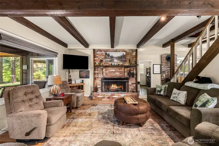 the living room features exposed wood beams, warm wood flooring, and expansive windows that frame tranquil water and forest views the living room features exposed wood beams, warm wood flooring, and expansive windows that frame tranquil water and forest views