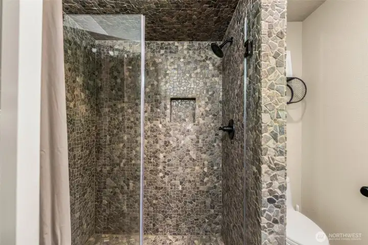 Custom walk-in shower featuring floor-to-ceiling river rock tile, a frameless glass enclosure, and dark bronze fixtures. Rich natural textures and artisan finishes create a spa-like atmosphere that complements the home's mountain setting. Custom walk-in shower featuring floor-to-ceiling river rock tile, a frameless glass enclosure, and dark bronze fixtures. Rich natural textures and artisan finishes create a spa-like atmosphere that complements the home's mountain setting.