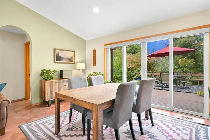 Bright, open-concept living and dining space featuring vaulted ceilings and large sliding doors that create a seamless connection to the expansive deck and surrounding greenery. Bright, open-concept living and dining space featuring vaulted ceilings and large sliding doors that create a seamless connection to the expansive deck and surrounding greenery.