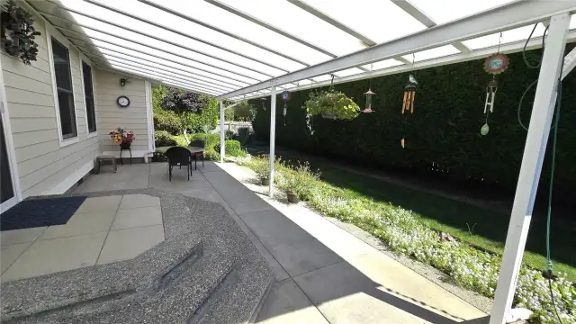 Covered back patio with light filtering cover and aggregate concrete patio. Very private with open area behind the hedge trees & fence.