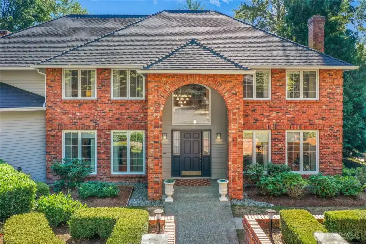 The grand entryway immediately impresses with a soaring arched brick portico and detailed trimwork, offering a glimpse into the craftsmanship and timeless style that defines this home. A welcoming walkway leads guests directly to the double front doors, creating a lasting first impression.