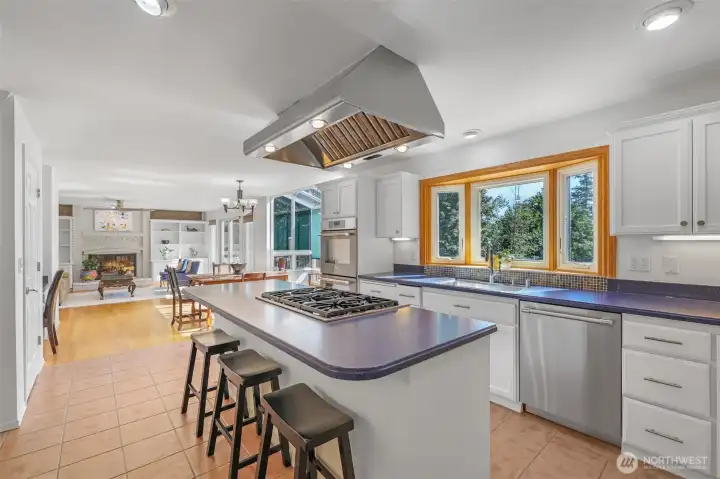 The expansive kitchen is designed for both function and style. With a center island featuring a gas cooktop, abundant cabinetry, double ovens, and stainless appliances, this space is ready for preparing meals of any scale. A large window over the sink frames serene views of the surrounding trees.