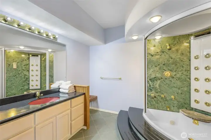 The adjacent lower-level bathroom offers a spa-like experience with a jetted tub, multiple shower sprays, and stylish finishes, adding luxury and convenience.