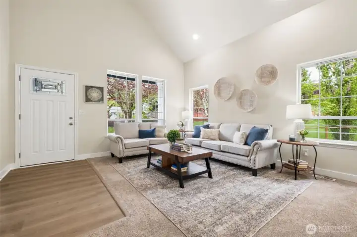 The formal living room offers a bright, comfortable space ideal for hosting guests or relaxing with a book. Large windows frame views of the serene property while vaulted ceilings amplify the natural light and create a warm, inviting atmosphere.