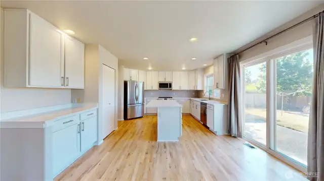 Updated kitchen featuring white shaker-style cabinetry, sleek stainless steel appliances, and a large center island with quartz countertops and ample drawer storage.
