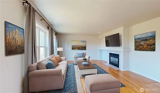 Warm and inviting family room filled with natural light from large windows. Beautiful hardwood floors flow throughout the space and a double-sided gas fireplace with a custom mantel serves as the focal point, adding both charm and functionality. Photo is virtually staged.