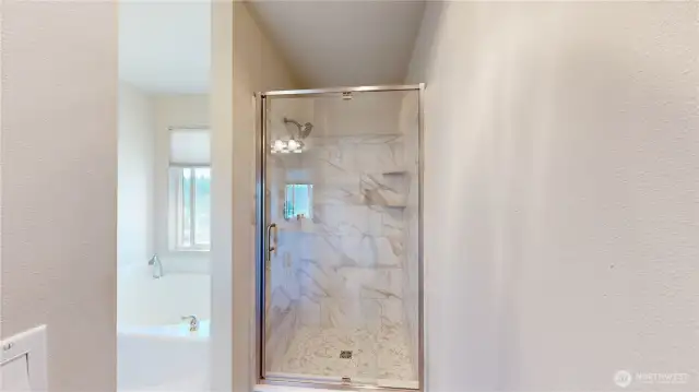 Tiled walk-in shower in the primary suite, featuring a glass enclosure, modern fixtures, and built-in shelving.