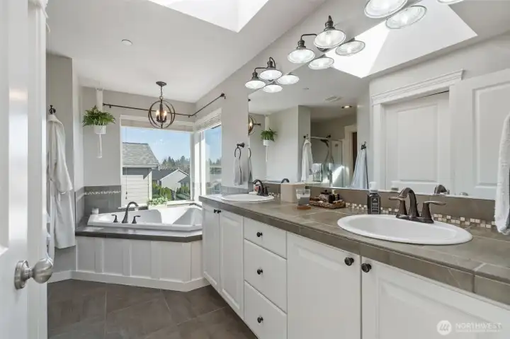 Gorgeous primary bath with double sinks, soaking tub, separate shower, toilet room and a large walk-in closet all lit up beautifully with a brightly lit skylight!