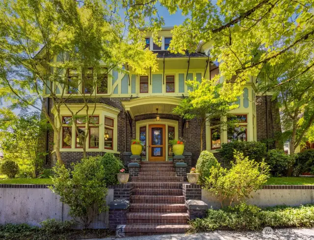 A stately brick staircase leads to the front door of this beautifully preserved 1909 Tudor, framed by mature trees and lush landscaping.