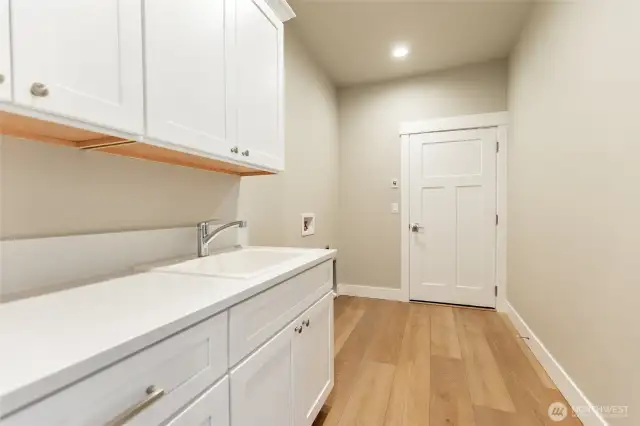 Large laundry area leading into garage with sink, counter space and cabinets for storage