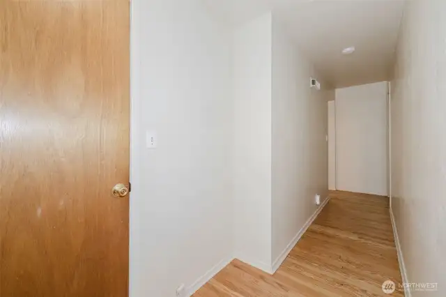 The hallway creates a smooth flow between living areas and bedrooms, offering wall space for artwork or photos and easy access to the full bath and storage closets. Original hardwood continues through the hall, reinforcing the warm, unified aesthetic throughout the home.