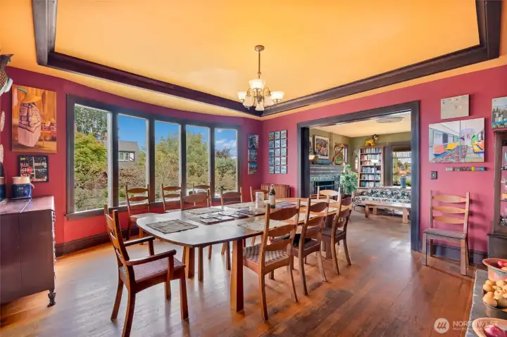 Dining room opens to the living room with large picture windows, coffered ceiling, time-appropriate chandelier, and abundant natural light.