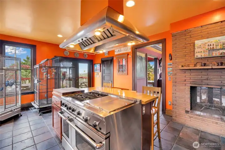 Chef's kitchen featuring a professional stainless steel range, dramatic hood, and classic brick fireplace — modern updates with timeless character.