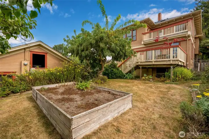Lush backyard with raised garden bed, mature plantings, and a view of the back deck — perfect for outdoor living and gardening.