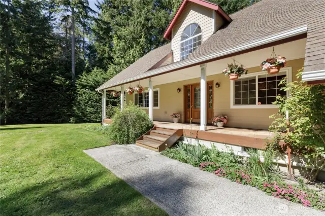 The Large front porch with a view of the expansive lawn and tree-lined lot as well as to the enclosed gardening space, trail and "sledding hill".