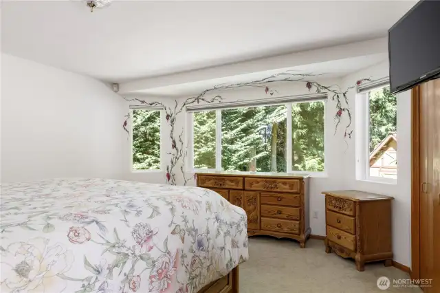 Primary suite on main level with 2 closets, view to backyard trees and playhouse, large windows with hand-painted wall art by Langley artist, Darla Neilson