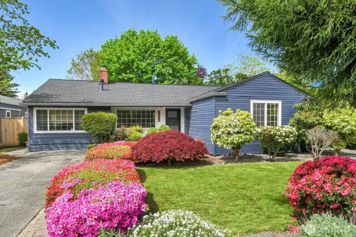 Welcoming front exterior with manicured yard, flowering shrubs, and timeless single-level living in desirable neighborhood.