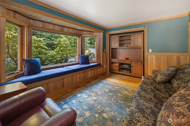 The den/office on the main level with bay window seat, warm wood paneling and wide planked wood floors.