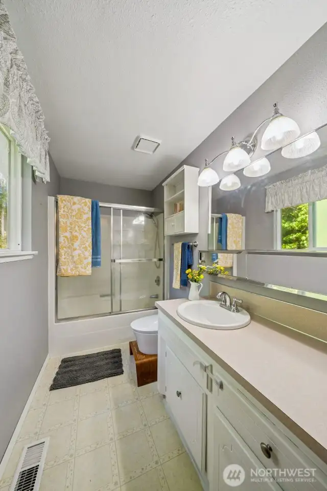 The full primary bath includes a glass sliding shower door, extra cabinet storage and sliding mirrored toiletry shelf below the vanity mirror.