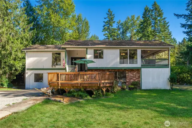 Inviting split-level exterior framed by mature trees, with a spacious front deck perfect for outdoor seating and curb appeal that blends brick and wood siding.