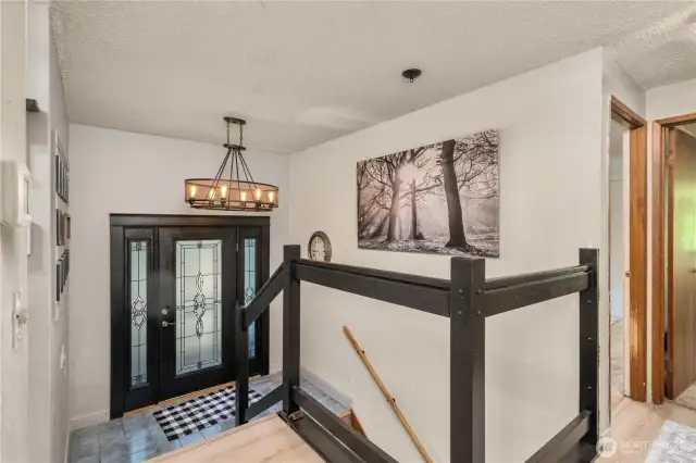 Bright split-entry foyer with decorative glass double doors and a contemporary chandelier, offering access to both levels of the home.