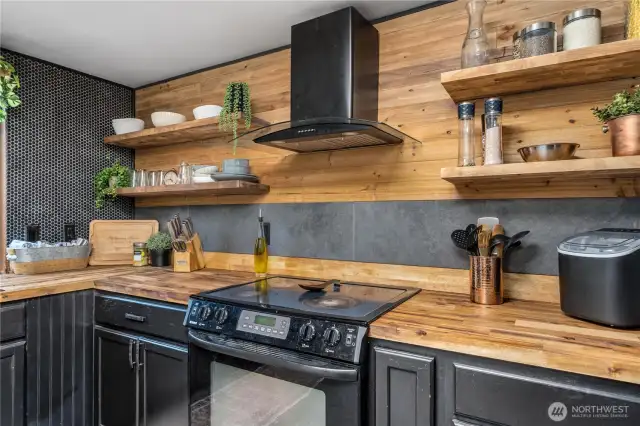 Stylish cooking space with tile backsplash, wood counters, and vent hood accented by open wood shelving.