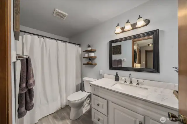 Updated full bathroom featuring a marble-look vanity, modern lighting, and open wood shelving for added style and storage.