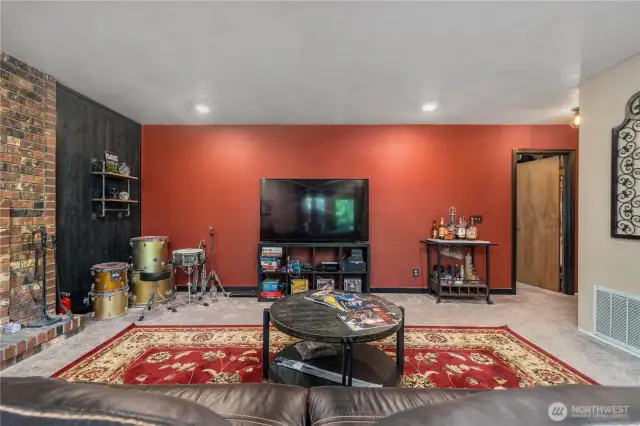 This vibrant recreation room offers plenty of space for entertainment and relaxation, featuring a bold red accent wall, built-in shelving, and a designated area for games and music. The layout is perfect for hosting movie nights, jam sessions, or casual gatherings with friends and family.