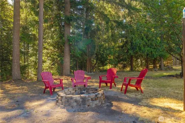 Nestled among mature evergreens, this inviting fire pit area offers a cozy retreat for evenings under the stars. The surrounding natural landscape provides a peaceful, private setting perfect for gathering with friends or enjoying quiet moments outdoors.