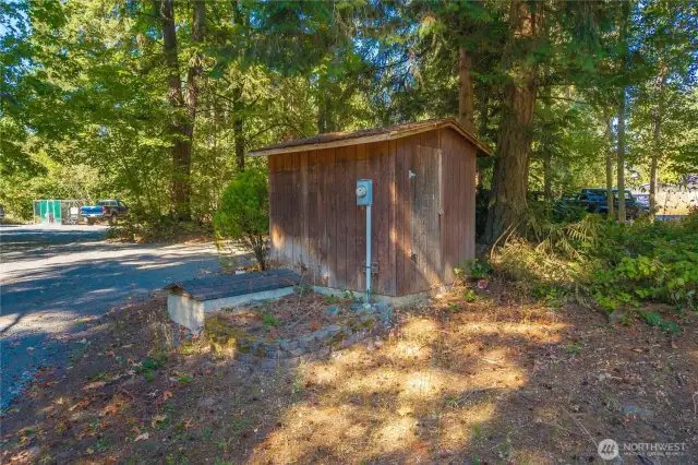 Rustic well house providing essential utility support for the property, set among mature trees for natural shade and protection.