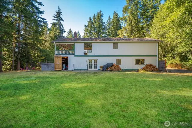 Rear view of the home showcasing its spacious layout, French door access to the backyard, and a covered upper-level porch overlooking the lawn. A convenient storage area beneath the covered porch offers additional space for tools, equipment, or seasonal items.